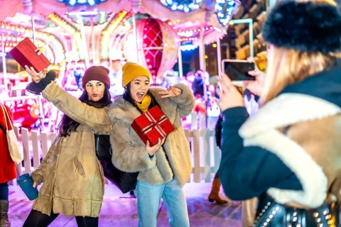 Three happy women posing with christmas gifts in front of carousel at night in a christmas market