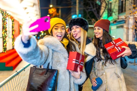 Three happy female friends taking a selfie while holding christmas gifts, enjoying a night out at a