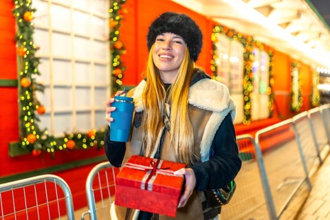Young woman enjoying christmas spirit at a decorated outdoor market, holding a christmas present