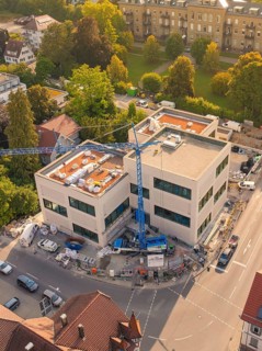 Large modern building under construction with a crane surrounded by an urban environment, small