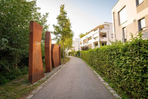 Rustic sculptures along a footpath through modern residential buildings, small town of Perle