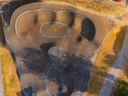 Pump track with blue lines seen from the air, surrounded by shadows and asphalt, pump track,