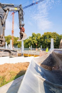 Excavator working on a construction site against a clear sky and trees in the background, car park