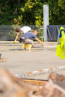 Workers bend over a concrete surface and use tools on a construction site, car park construction,