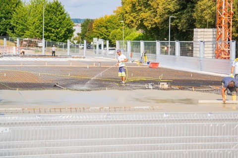 Construction workers working on the concrete surface, surrounded by trees, with safety fences, car