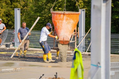 Construction workers unloading concrete with a large hopper on a building site with metal