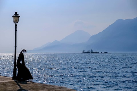 Sculpture of a fisherwoman at the harbour of Cassone di Malcesine, in the background Isole di