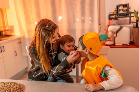 Children wearing pumpkin costumes celebrating halloween joyfully with their mother at home,