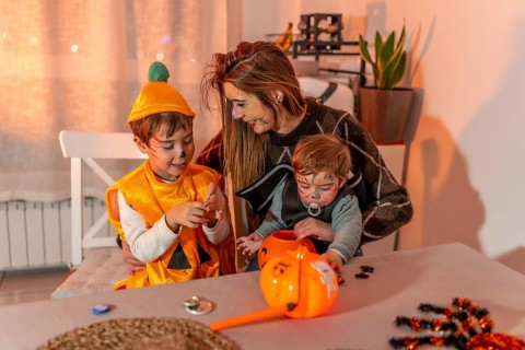 Mother and children with painted faces wearing halloween costumes are playing at home with pumpkin