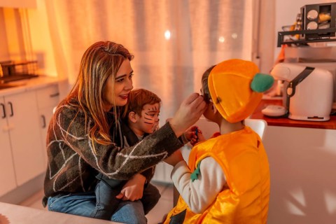 Mom applying makeup on her kids, joyfully preparing costumes for halloween night, creating fun