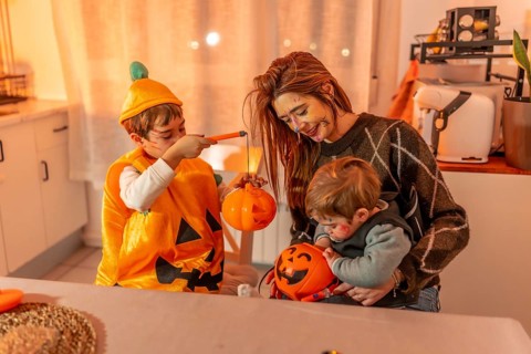 Children and mother painting halloween pumpkins, wearing costumes, and making decorations at home