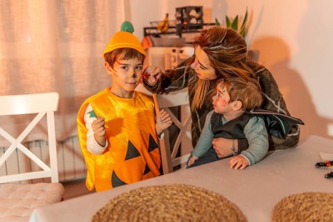 Mother painting her children's faces with halloween makeup, preparing for trick or treating