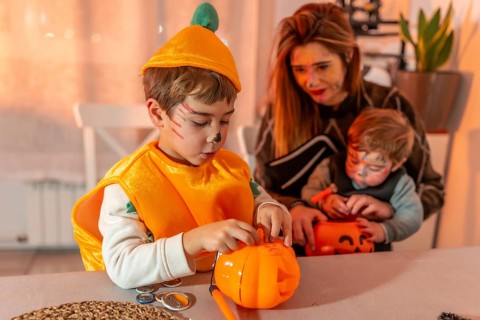 Children wearing halloween costumes are decorating pumpkin baskets with their mother at home