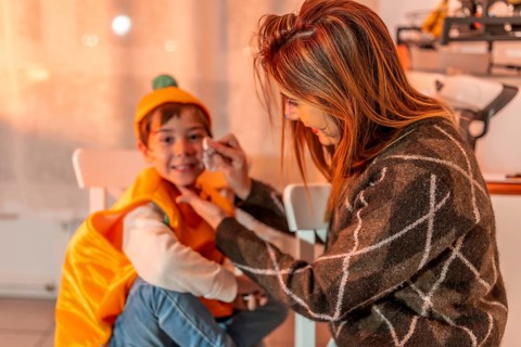 Mom applying colorful makeup on her son's face, creating a festive atmosphere for their halloween