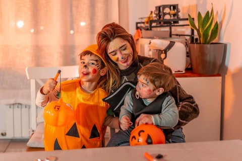 Mom and her kids are smiling, wearing halloween costumes and makeup, holding pumpkin buckets and