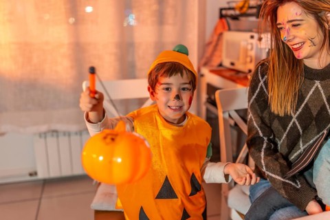 Happy child wearing pumpkin costume holding a plastic jack o' lantern celebrating halloween with