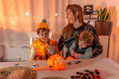 Mother and her two children wearing halloween costumes and makeup, playing with candies on a table