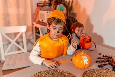 Children with painted faces preparing halloween pumpkin decorations at home, with their mother