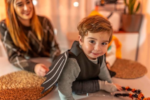 Smiling toddler wearing a bat costume crawling on a table while getting ready for a halloween party