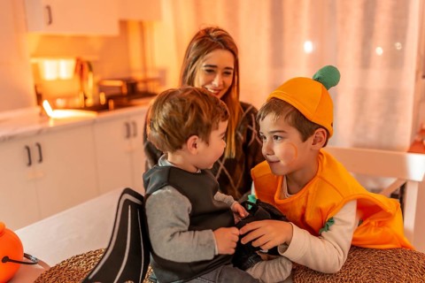 Two young brothers wearing halloween costumes playing together at home, watched by their smiling