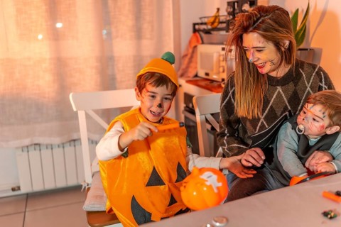 Happy children with painted faces wearing halloween costumes painting pumpkins with their mother at