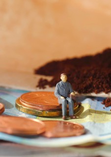 Miniature figure of a man sitting on coins and banknotes, ground coffee in a filter bag in the