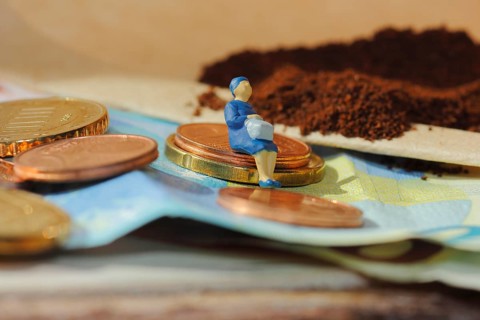 Miniature figure of a woman sitting on coins and banknotes, ground coffee in a filter bag in the