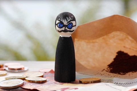 Male wooden cone figure with coins and banknote in front of filter bag with coffee North