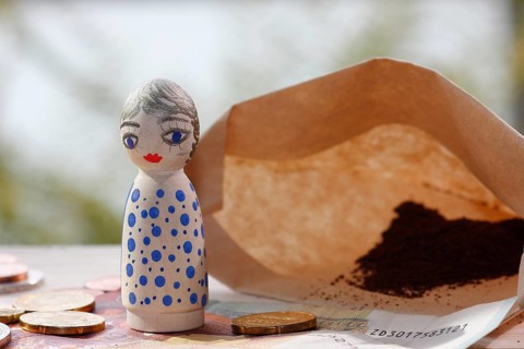 Pretty female wooden cone figure with coins and banknote in front of filter bag with coffee North