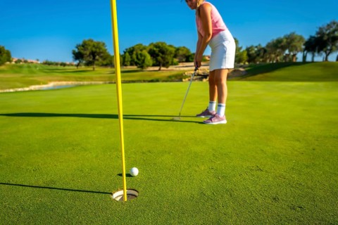 Woman skillfully putting on a golf course, aiming for the hole under a clear blue sky. Lush green