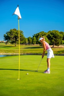 Female golf player putting the ball on the green under a bright sun, showcasing skill and