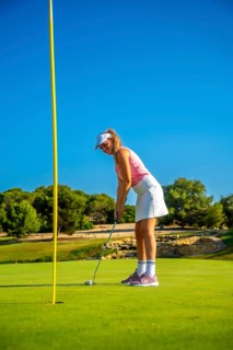 Female golfer putting the ball on the green under a bright sun, showcasing skill and precision on