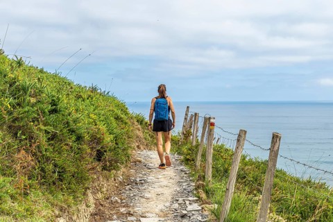 Female tourist walking along a coastal path in zumaia, basque country, enjoying the scenic view of