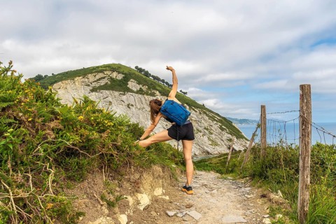 Female hiker stretching leg on a trail overlooking sakoneta beach and flysch cliffs in zumaia,