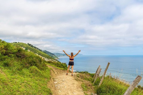 Woman hiker celebrating scenic coastal view with raised arms at sakoneta beach flysch cliffs in