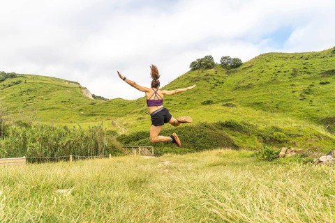 Sporty woman jumping with outstretched arms in a beautiful natural landscape in zumaia, gipuzkoa,