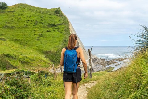 Female tourist walking down a path towards sakoneta beach, enjoying the view of the flysch cliffs