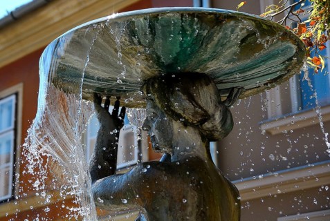 Water flowing from a basin held by a beautifully crafted statue, creating dynamic jets and splashes