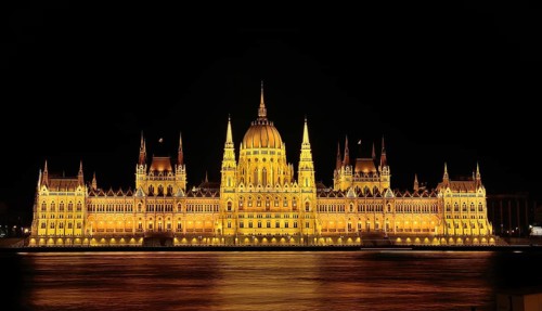 Majestic hungarian parliament building glowing gold at night, reflected in the danube river,