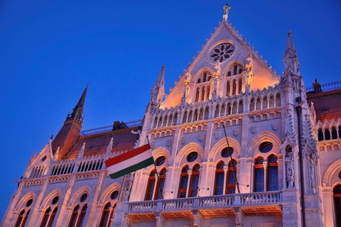 Ornate facade of hungarian parliament building illuminated at twilight with hungarian flag waving,