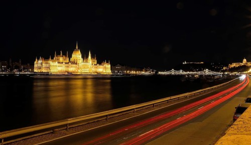 Light trails illuminating road by danube river with hungarian parliament building reflecting on