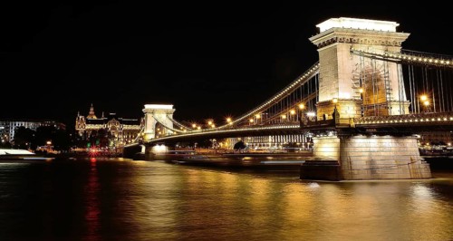 Chain bridge reflecting on danube river with gresham palace in background at night, budapest,