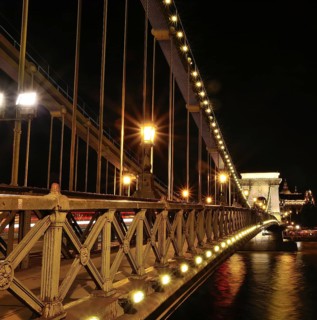 Chain bridge glowing beautifully at night, showcasing blurred car light trails against the backdrop