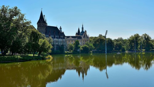 Vajdahunyad castle reflecting beautifully on the lake in budapest's city park, surrounded by lush