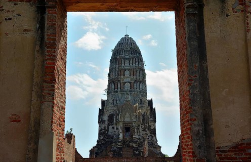 Crumbling brick walls frame a majestic ancient prang under a partly cloudy sky, showcasing the rich