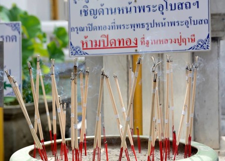 Incense sticks are burning, creating a fragrant smoke, in a pot at a temple in thailand,