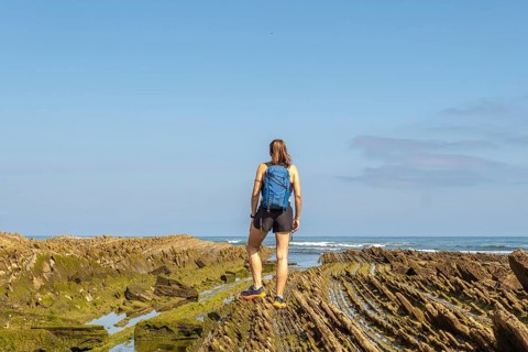 Female hiker with backpack admiring the stunning coastal rock formations of the zumaia flysch on