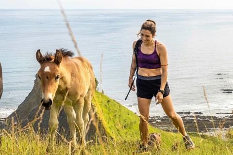 Female hiker with her dog encountering wild horses while walking on the cliffs of sakoneta beach,