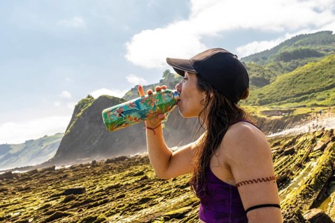 Female athlete hydrating after exercising on sakoneta beach, enjoying breathtaking views of zumaia