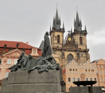 Jan hus monument standing tall in old town square, with the iconic tyn church rising majestically